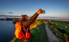Une voyageuse prenant un selfie face aux Falaises de Moher - © Tolo